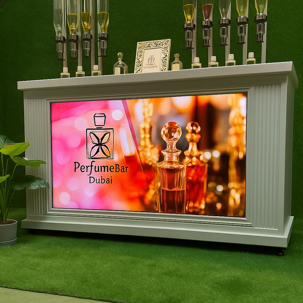 Perfume Booth setup in Dubai featuring a branded fragrance bar with colorful dispensers, interactive screen, and artificial grass backdrop for events and exhibitions